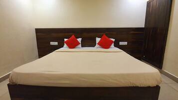 A hotel room with a large bed, dark wooden headboard, and two red pillows.