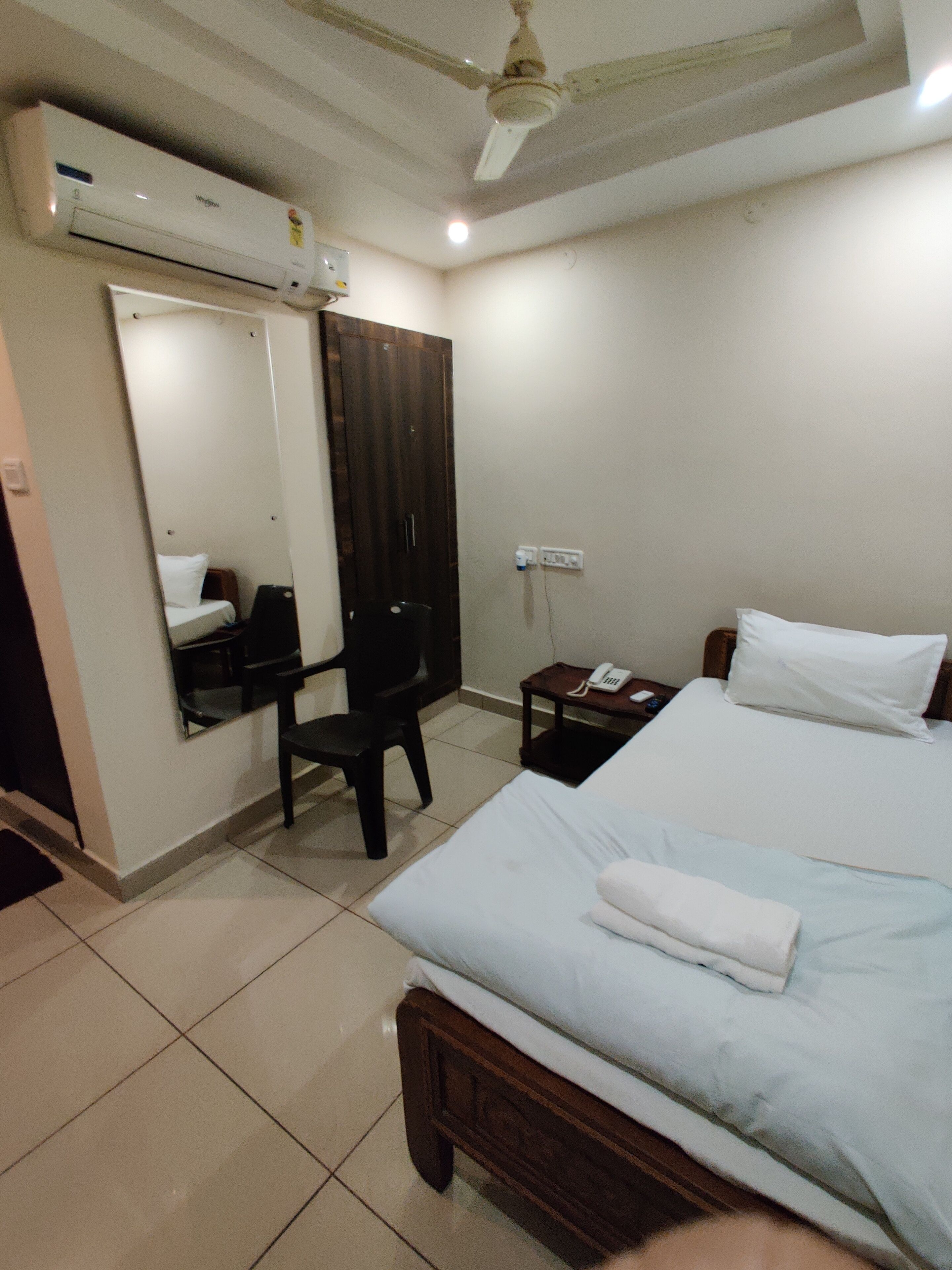 A hotel room with a bed, a desk, a chair, a wardrobe, and a ceiling fan.
