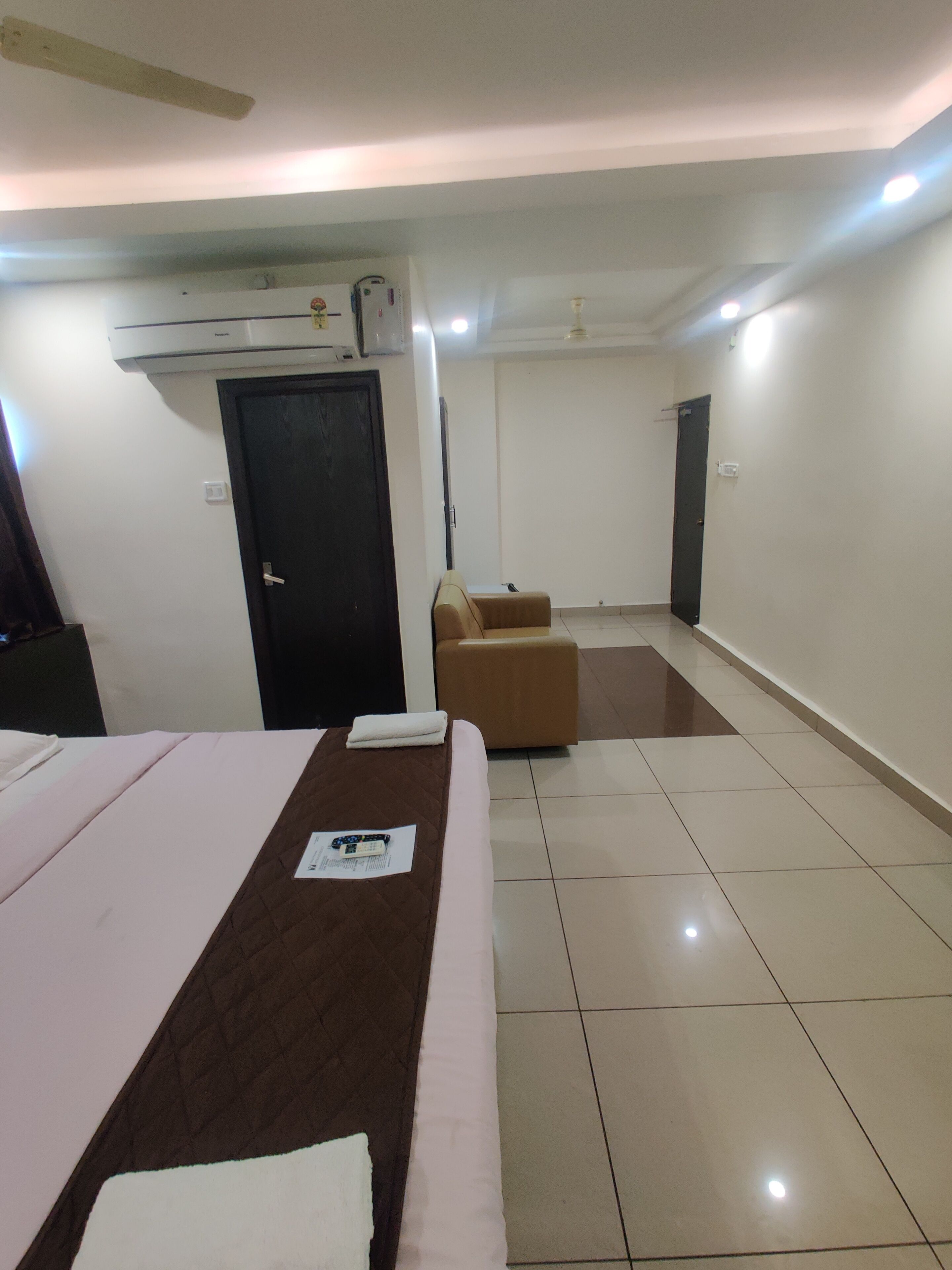 A hotel room with a bed, a small sofa, a door, and an air conditioning unit.
