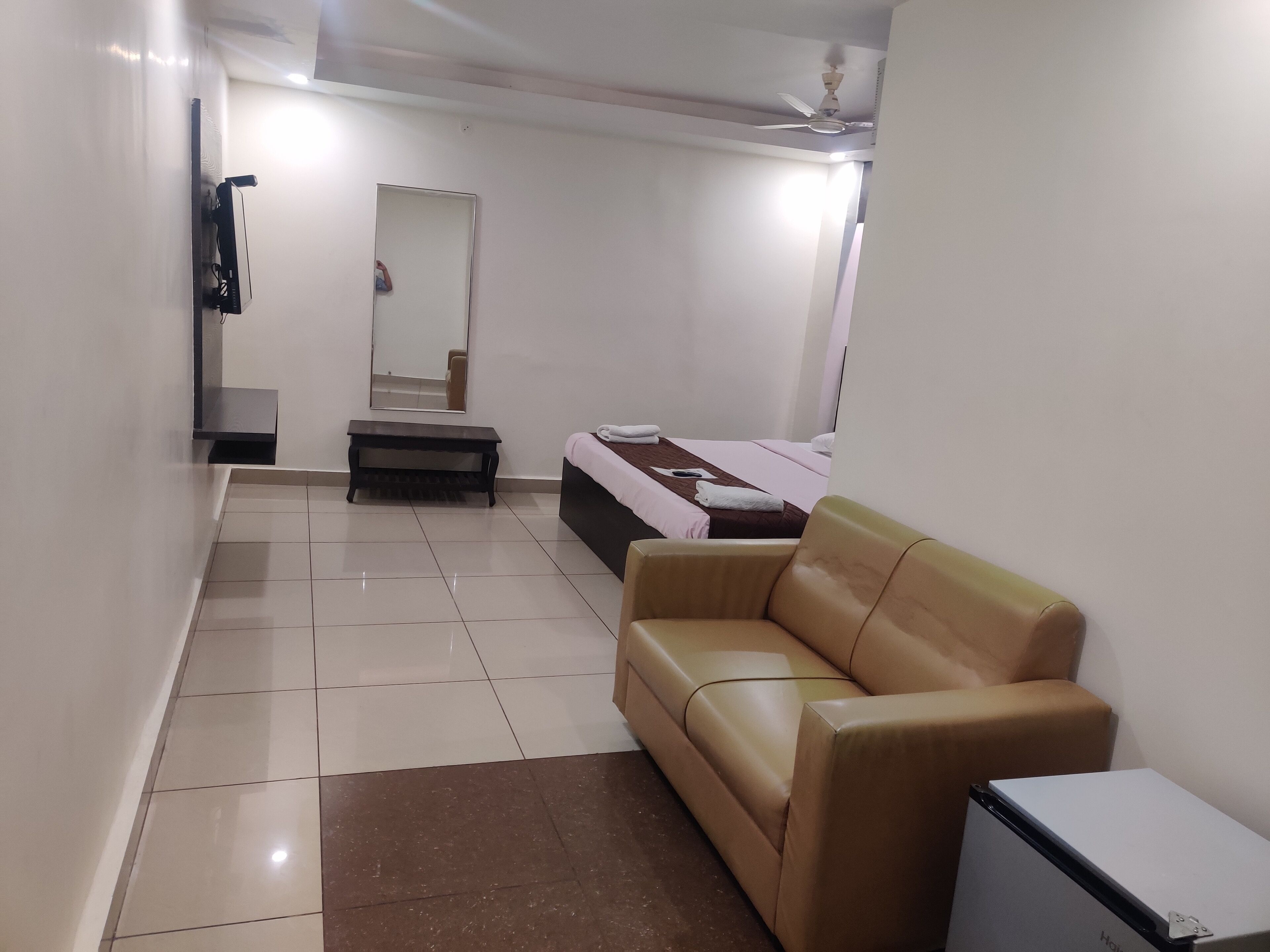 Habitación de hotel con sofá, cama, mesita, espejo y ventilador de techo.