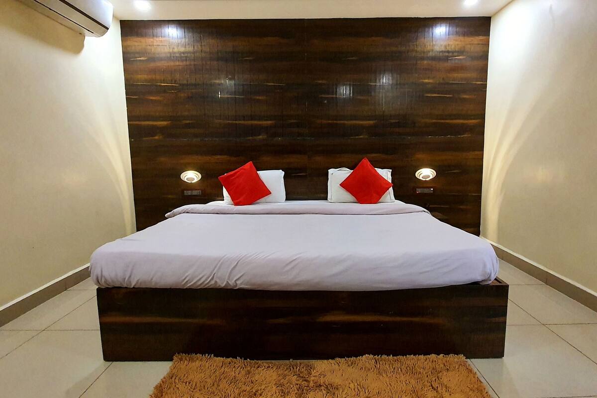 Ein modernes Hotelzimmer mit einem dunklen Holzkopfende, weißer Bettwäsche und zwei roten Kissen.