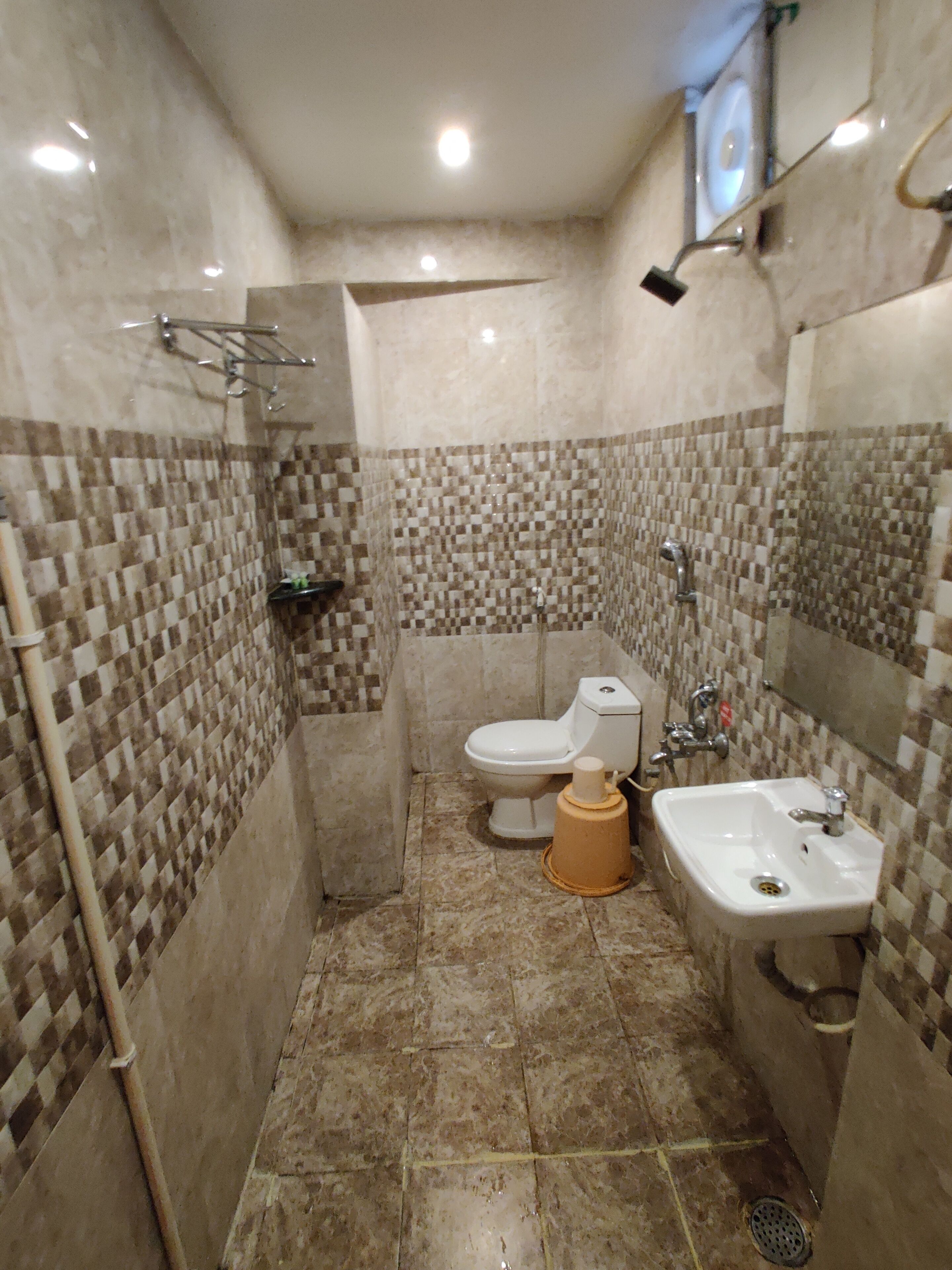 A bathroom with a tiled shower wall, a toilet, a sink, and a showerhead.