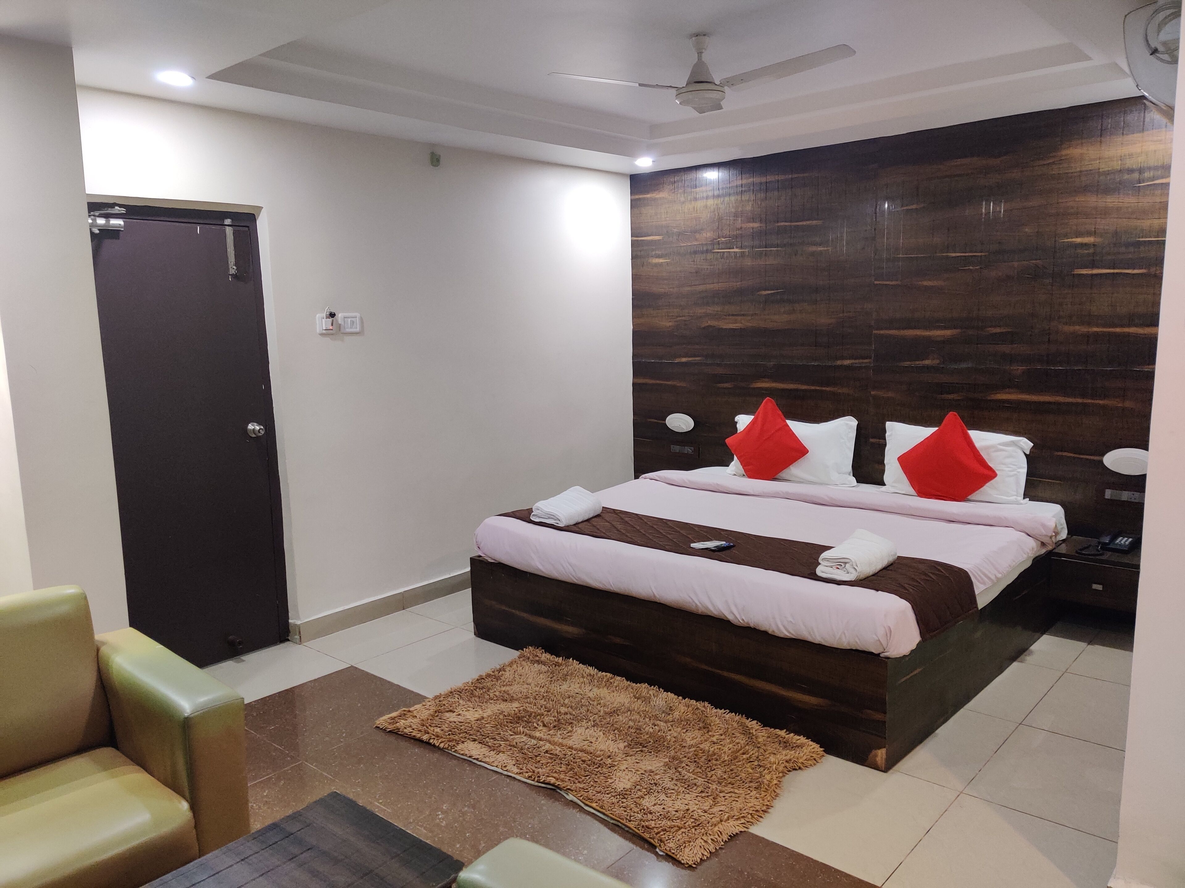 Habitación de hotel con cama, escritorio, silla, puerta y ventilador de techo.