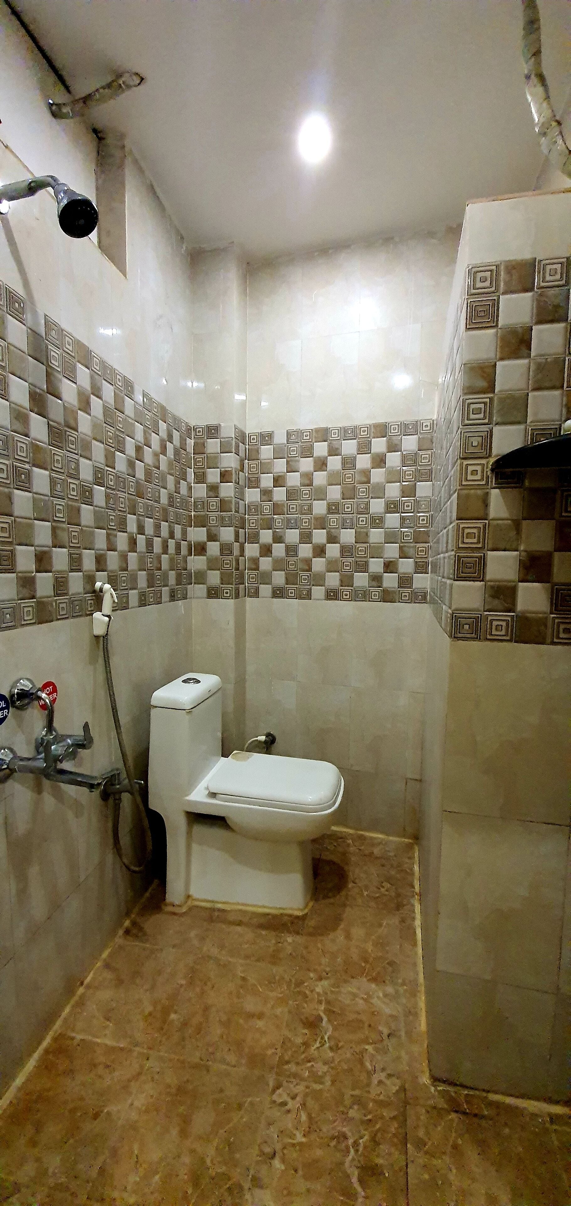 Casa de banho com sanita, chuveiro e paredes em azulejo.
