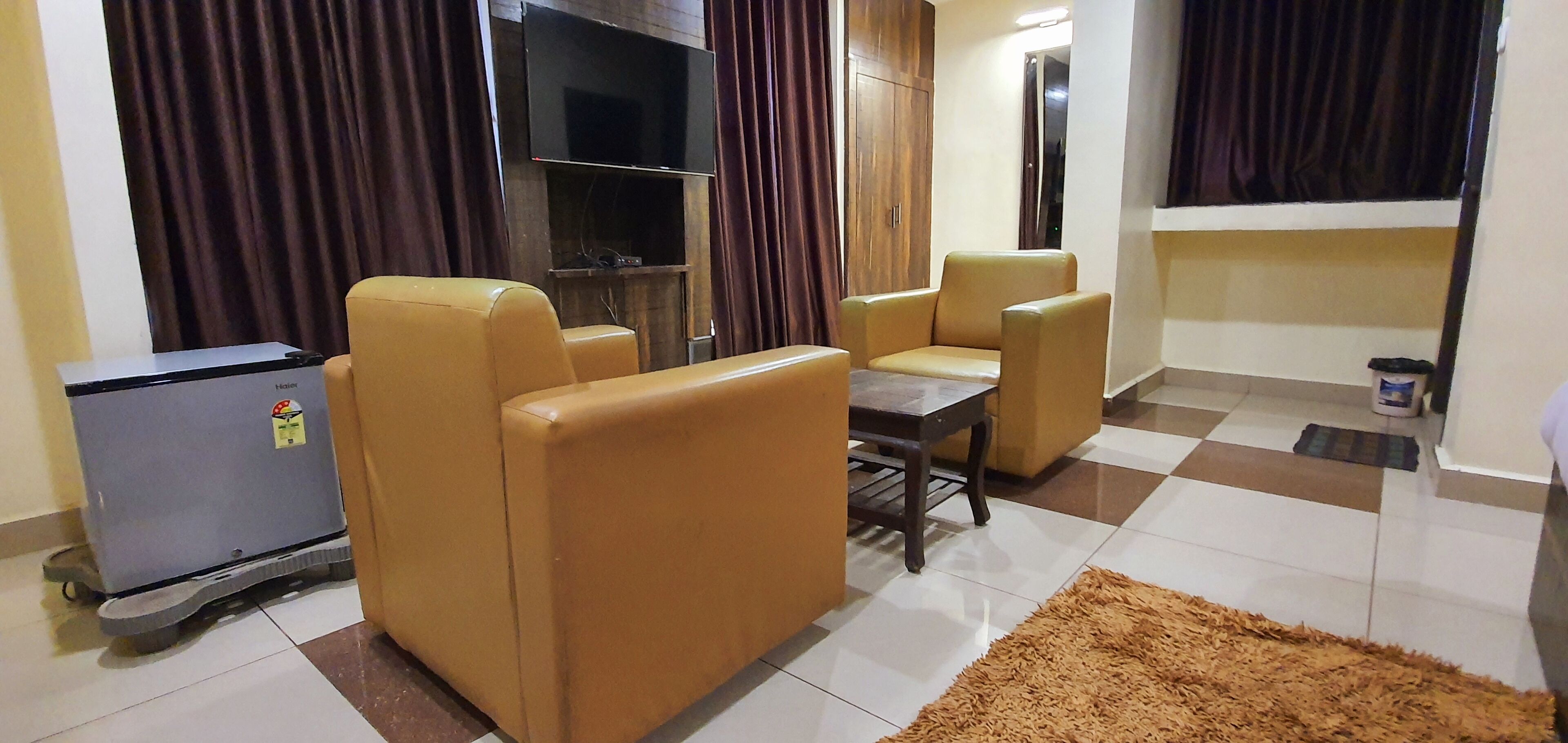 A living room with a sofa set, a coffee table, a TV mounted on the wall, and a small refrigerator.