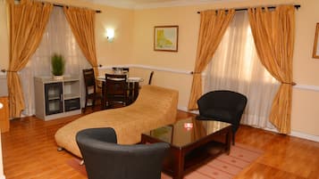 A furnished living room with a sofa, a coffee table, a chair, a small table with a lamp, and a potted plant.