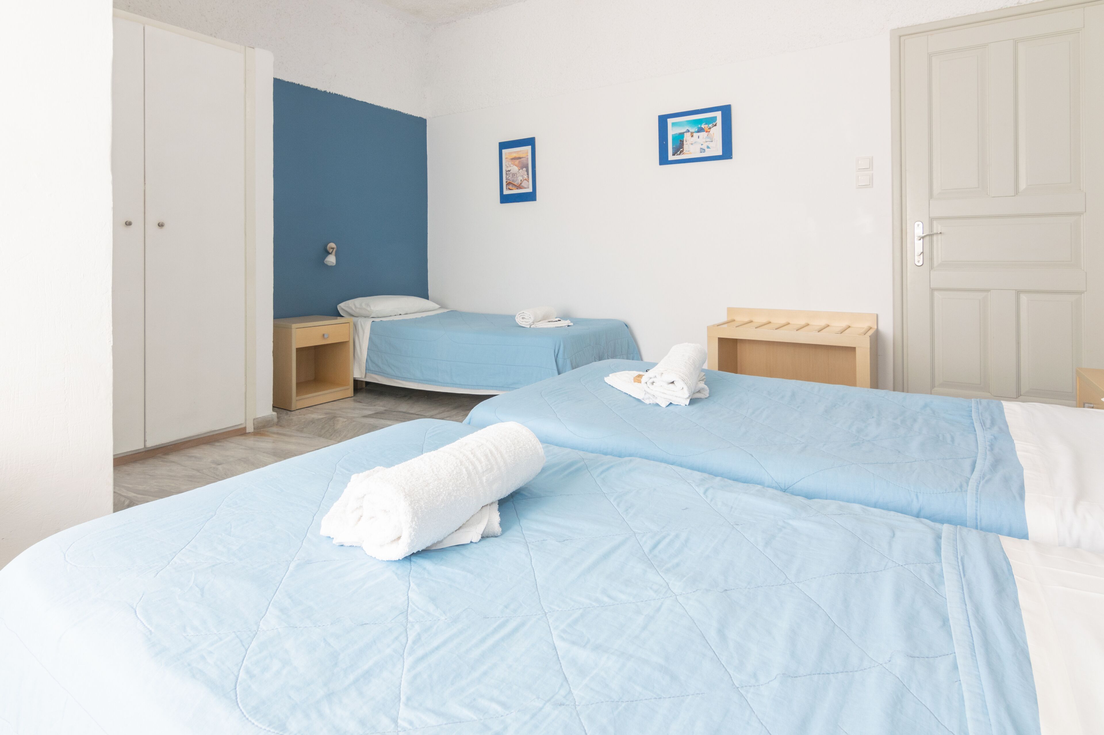 Une chambre d’hôtel avec deux lits, une armoire, une table de chevet et un mur orné de deux tableaux encadrés.