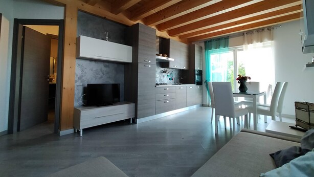 A modern kitchen with grey cabinets, a built-in oven, and a dining area with a white table and chairs. - Rome beach house (Fiumicino)