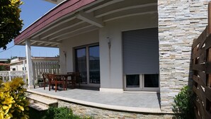 A covered outdoor patio with a table and chairs, stone walls, and a view of neighboring buildings. - Rome beach house (Fiumicino)