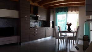 A modern kitchen with wooden beams, a dining area with white chairs, and a TV mounted on the wall. - Rome beach house (Fiumicino)