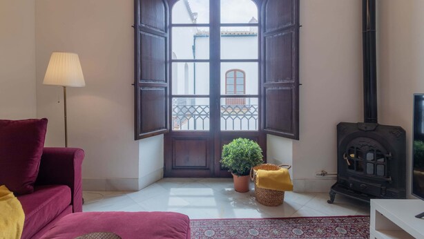 A room with a large arched window, a sofa, a lamp, a potted plant, a woven basket, and a wood-burning stove. - Córdoba Cool  Homes Vailima (Cordoba)