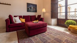 A living room with a red sofa, a patterned rug, a painting on the wall, and a window with a view of a building. - Córdoba Cool  Homes Vailima (Cordoba)