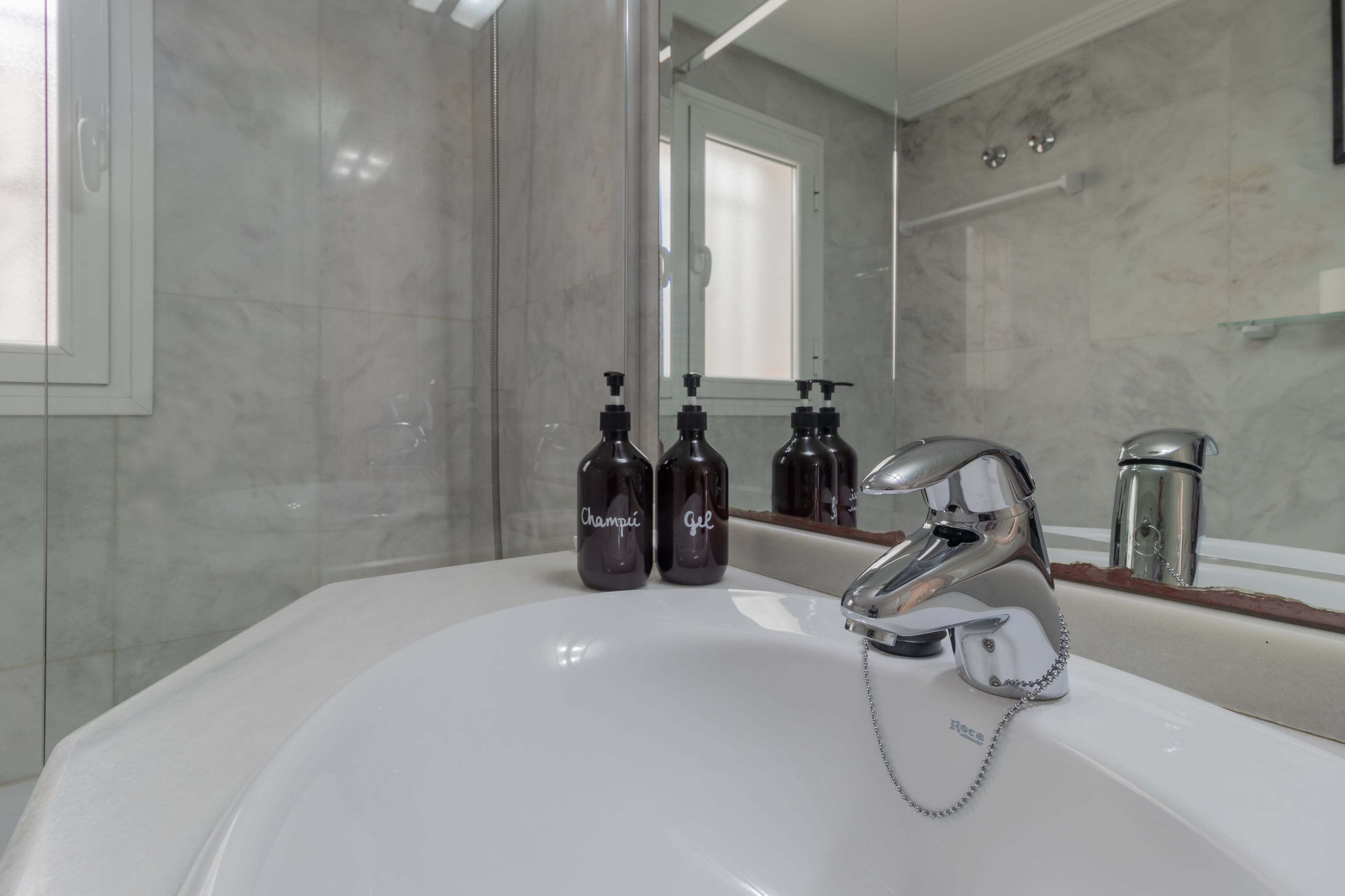 A bathroom with a white sink, chrome faucet, and two dark bottles labeled 'Champi' and 'gel' on the counter.