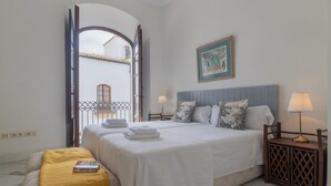 A hotel room with two beds, a wooden nightstand with a lamp, a painting on the wall, and a balcony with a railing. - Córdoba Cool  Homes Vailima (Cordoba)