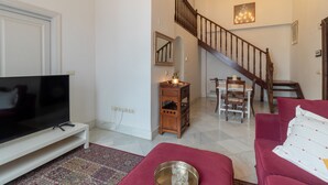 A living room with a TV, red sofa, patterned rug, wooden side table, and a staircase leading to another room. - Córdoba Cool  Homes Vailima (Cordoba)
