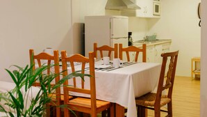 A dining area with a table set for four, wooden chairs, a white tablecloth, and a white refrigerator in the background.