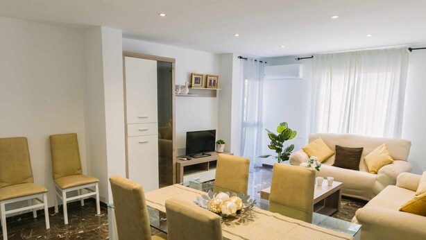A modern living room with a glass dining table, beige chairs, a sofa, and a TV. - Cordobacourt la Ribera (Cordoba)