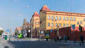 A street view with a yellow building, a green tram, and pedestrians. - Cordobacourt la Ribera (Cordoba)