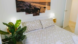 A neatly made bed with patterned bedding, a large wall-mounted sunset painting, bedside lamps, and a potted plant. - Cordobacourt la Ribera (Cordoba)
