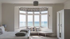 Een slaapkamer met een groot erkerraam, een bed met hoofdeinde, een bankje en een kledingkast.
