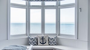 Een erker met uitzicht op zee, een witte bank en twee kussens met nautische motieven.
