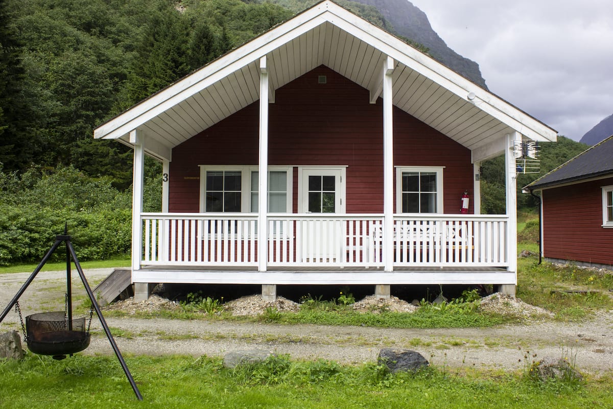 A red wooden house with a white porch and a swing set in front.