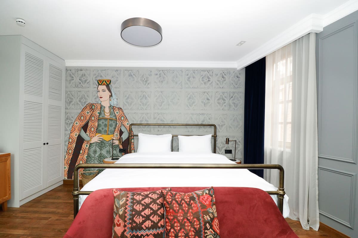 Classic hotel room with a neatly made bed, patterned wallpaper, and a wardrobe with a mirror.