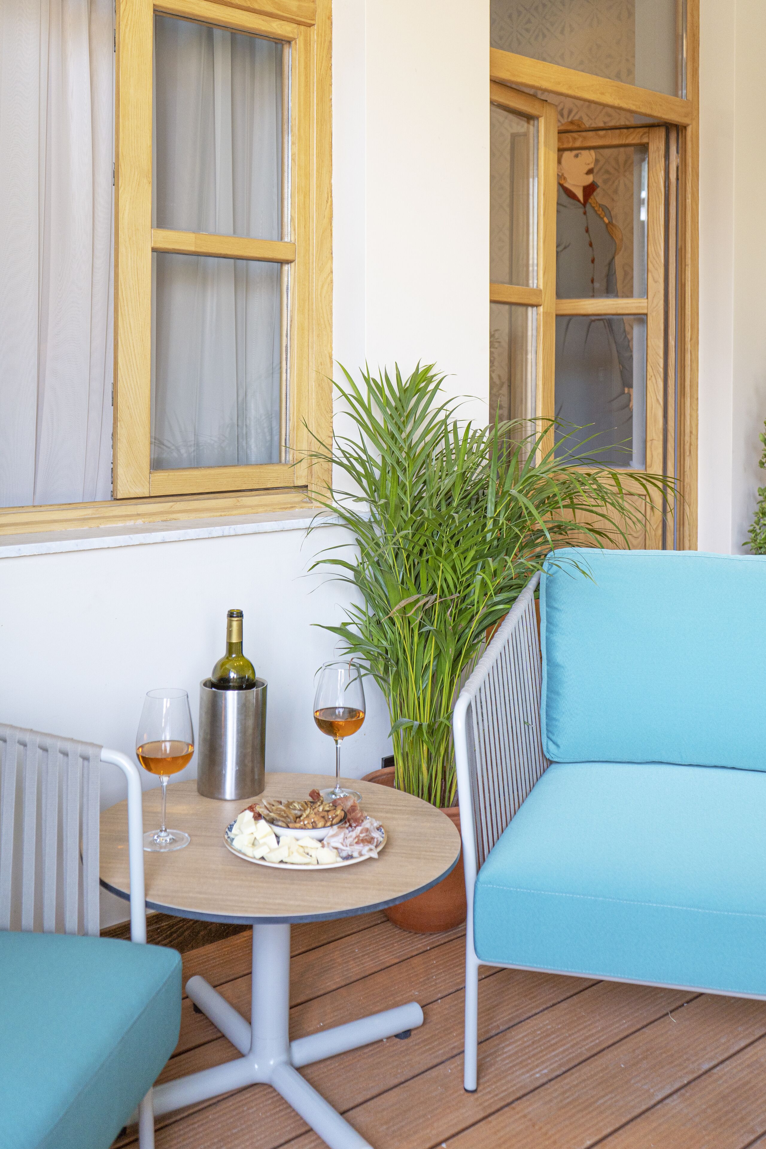 Een gezellig buiten zitgedeelte met een tafel, twee stoelen, een plant in pot en een raam met gordijnen.