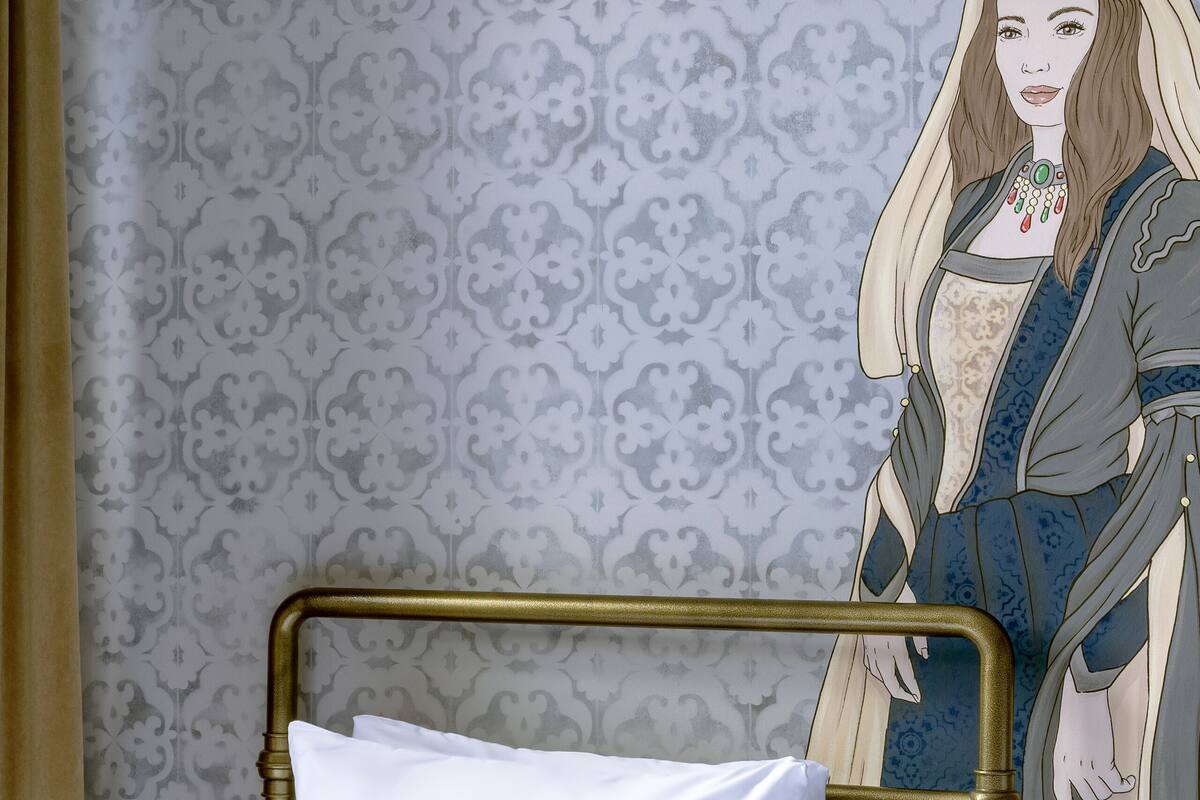 A hotel room with a bed, a metal headboard, and a patterned wallpaper.
