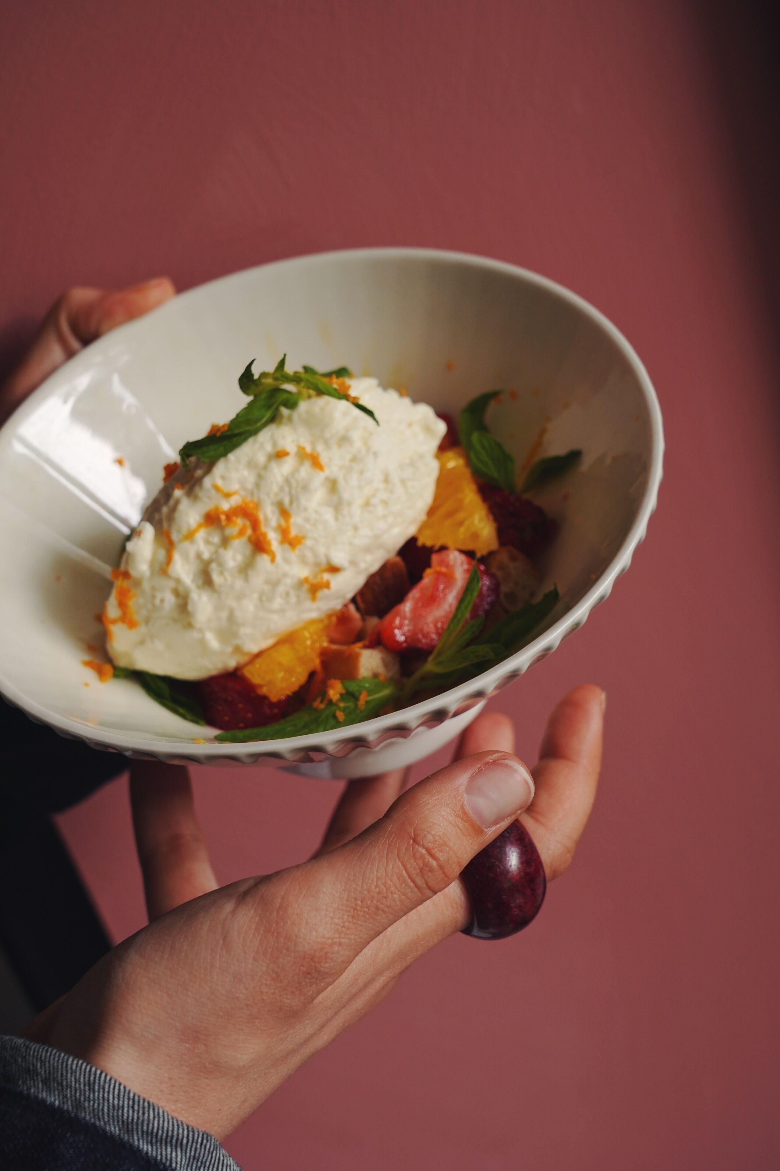 A person holding a bowl with a dessert and fruit salad.