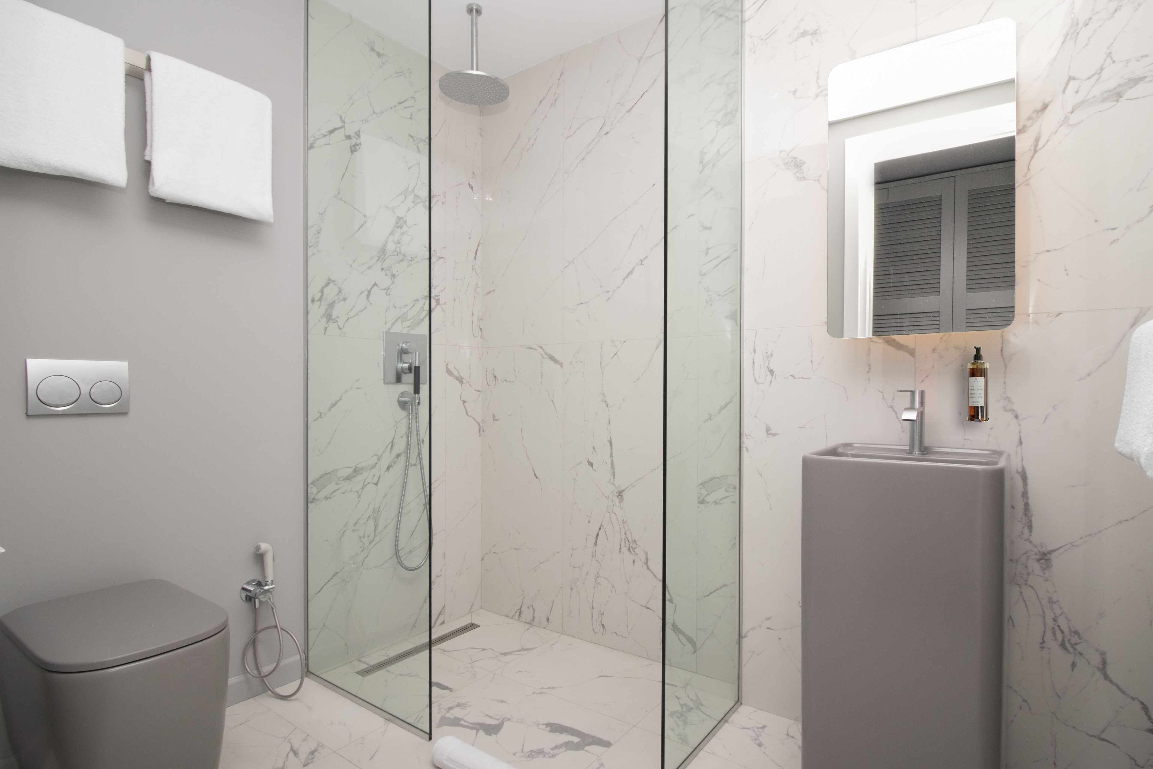 A modern bathroom with a glass-enclosed shower, a pedestal sink, and a marble-tiled floor.
