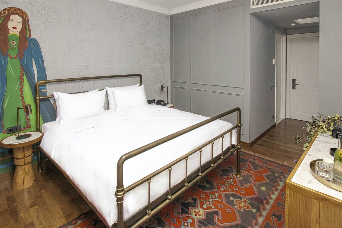 A neatly arranged bedroom with a metal-framed bed, a wooden nightstand, a decorative rug, and a nightstand lamp.