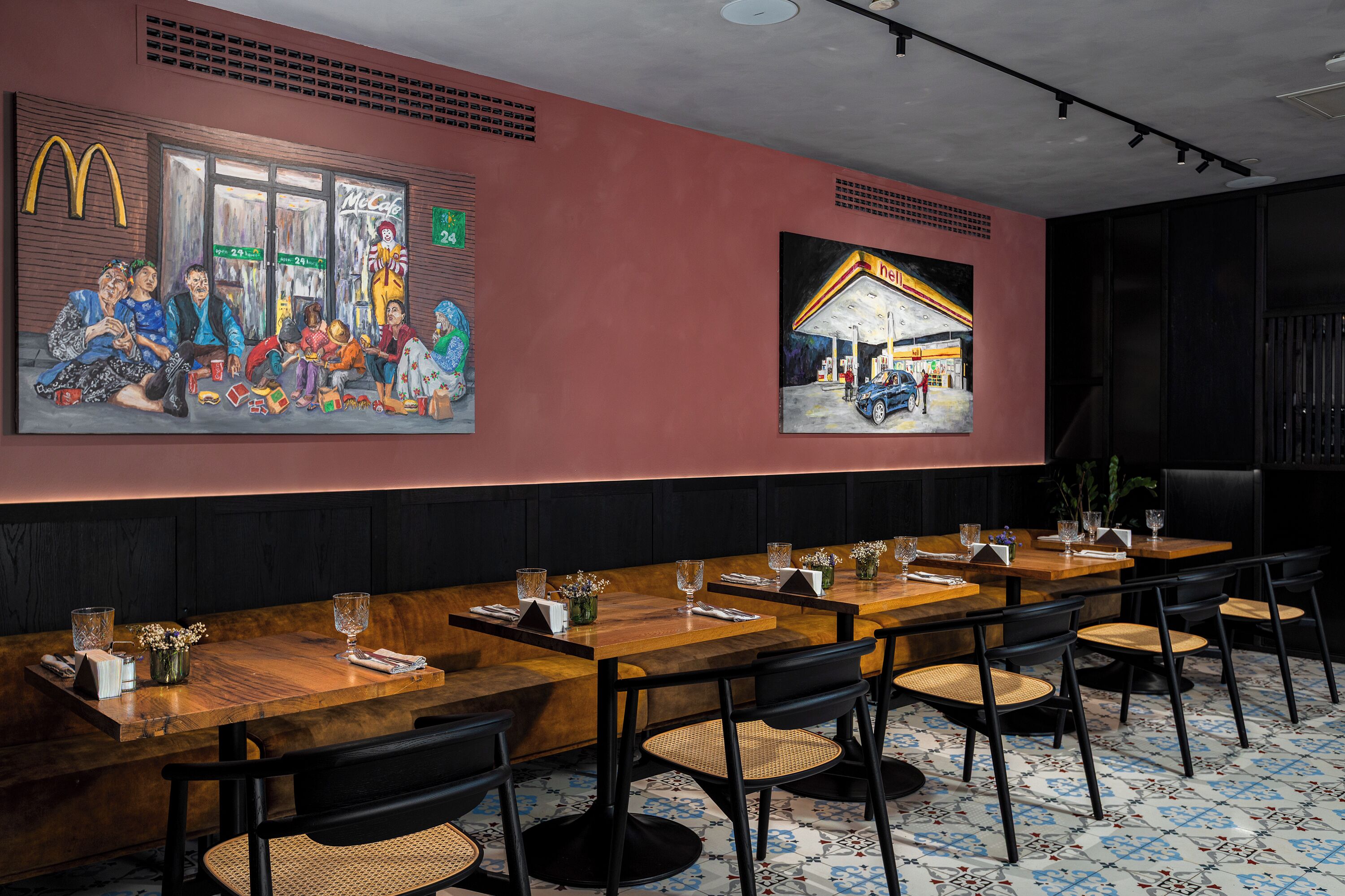 Ein Restaurant mit langen Holztischen, schwarzen Stühlen und einer roten Wand mit zwei großen Bildern.