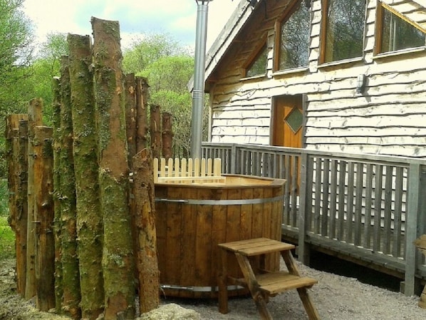 A rustic wooden cabin with a wooden hot tub and a wooden ladder leading up to it.