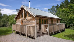 A wooden cabin with a metal roof, a deck, and a gravel driveway. - OAK is a charming, well equipped log cabin with hot tub and wood burning stove (Dalavich)