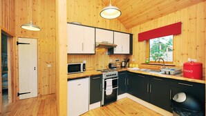 A compact kitchen with wooden walls, a microwave, stove, sink, and a red bread container. - OAK is a charming, well equipped log cabin with hot tub and wood burning stove (Dalavich)