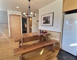 A wooden bench table in a room with a chandelier, a framed picture on the wall, and a refrigerator with a caution sign.