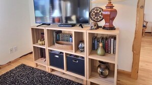 A living room with a flat-screen TV on a wooden stand, a lamp, bookshelves, and a black rug. - `Elk Ridge` | Hot tub, Wifi, Roku, Close to town. (Packwood)