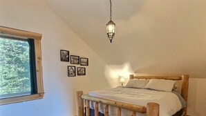 A bedroom with a wooden bed, a window with curtains, a hanging light fixture, and framed pictures on the wall. - `Elk Ridge` | Hot tub, Wifi, Roku, Close to town. (Packwood)