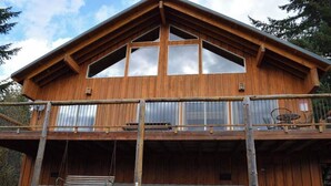 A wooden cabin with a balcony, large windows, and a swing. - `Elk Ridge` | Hot tub, Wifi, Roku, Close to town. (Packwood)