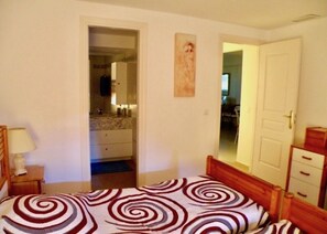 Une chambre à coucher comprenant un lit, une table de chevet, une commode et une porte donnant sur une autre pièce.