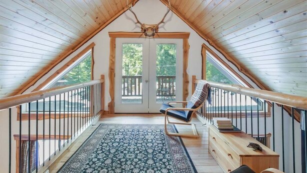 Interior de madera con techo inclinado, un ventanal y una silla junto a la ventana.