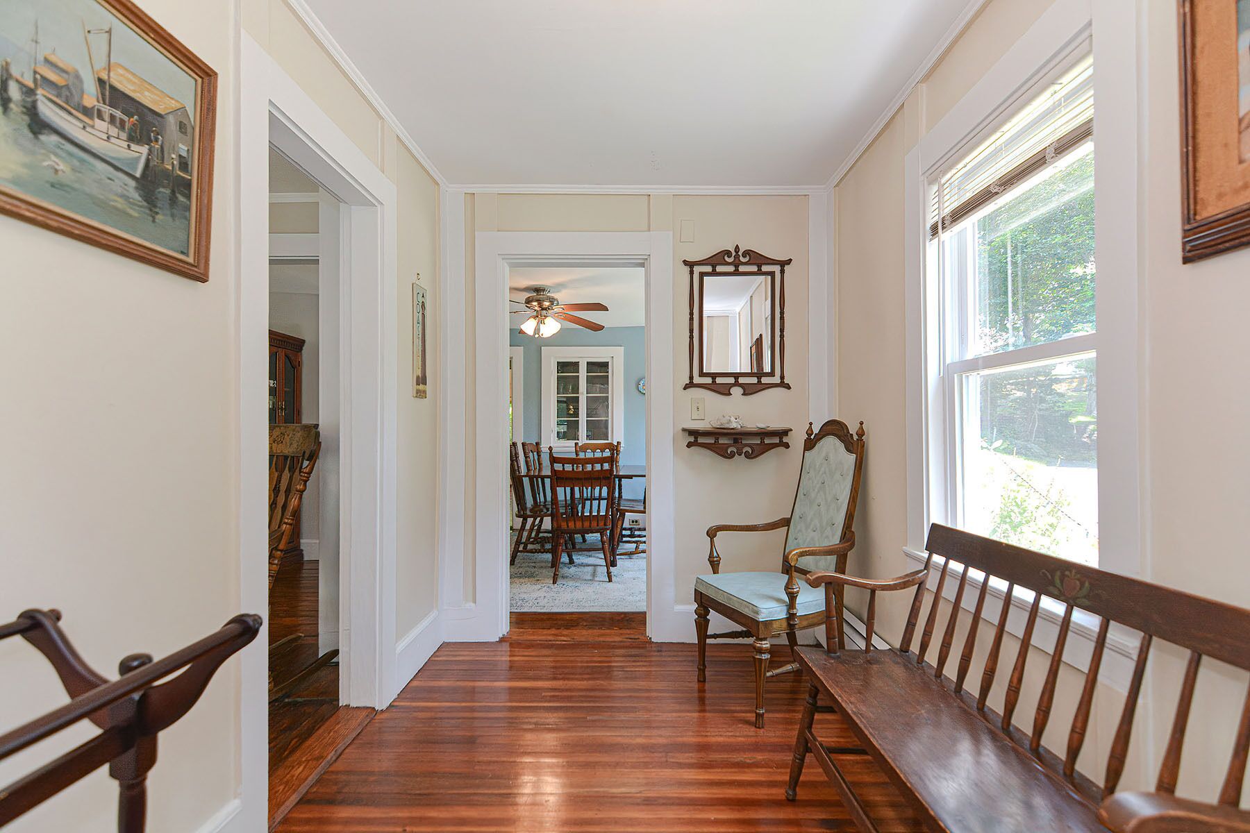 A hallway with wooden flooring, a dining area with a table and chairs, and a bench along the wall.