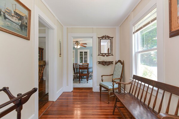 A hallway with wooden flooring, a dining area with a table and chairs, and a bench along the wall.