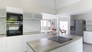 Une cuisine moderne avec des meubles blancs, un four encastré, un réfrigérateur et un coin repas comprenant une table et des chaises.