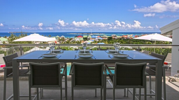 Une table à manger avec des chaises, donnant sur la piscine et offrant une vue sur la plage et les parasols.