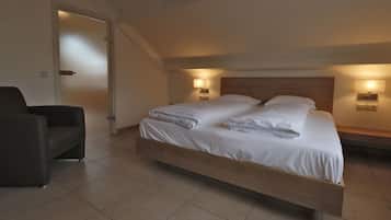 Un dormitorio moderno con una cama de madera, dos lámparas de noche, un sillón oscuro y una puerta que da a otra habitación.