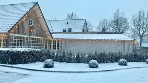 Un edificio de madera con techo inclinado, rodeado de arbustos y árboles cubiertos de nieve.