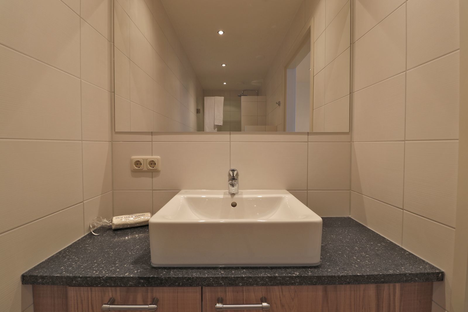 A bathroom with a white sink, dark granite countertop, and wooden cabinets.