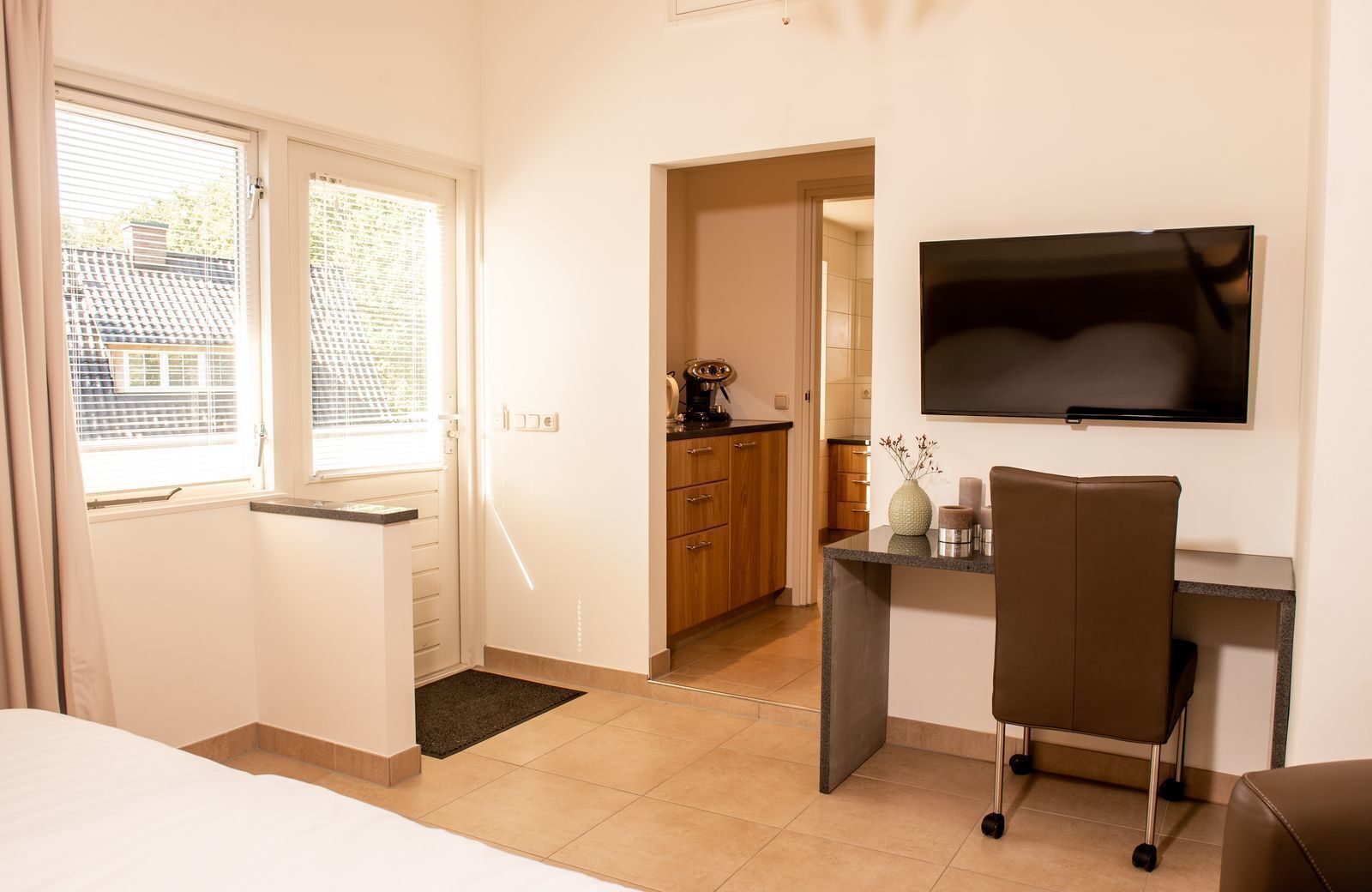Ein Hotelzimmer mit Bett, Schreibtisch mit Stuhl, Fernseher und Blick ins Freie.